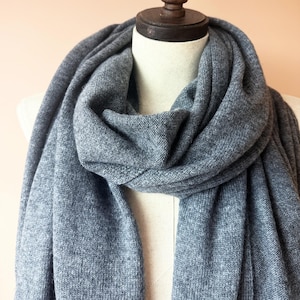 May include: A soft, gray scarf draped over a mannequin. The scarf is made of a knitted material and has a simple, classic design. The fabric appears to be warm and cozy, perfect for cooler weather.