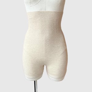 May include: Beige-colored shapewear shorts with a high-waisted design. The shorts are displayed on a mannequin and feature a ribbed texture on the waist area. The shorts are designed to provide support and shaping.