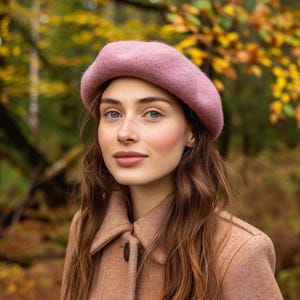 May include: A woman wearing a pink beret and a brown coat. She has long brown hair and is looking at the camera.