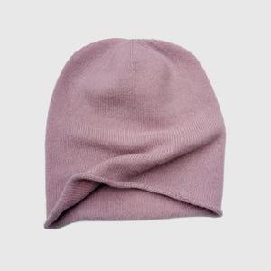 May include: A solid mauve-colored beanie hat. The hat is made of a soft knit material and has a slightly slouchy fit. The hat is a solid color and has a simple, classic design, suitable for cold weather.