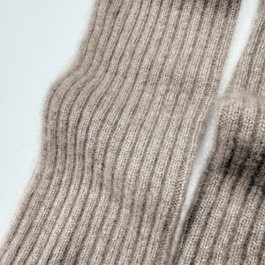 May include: Close-up of two light brown ribbed knit socks. The socks are made of a soft, textured material and are folded. The ribbed design runs vertically along the length of the socks.