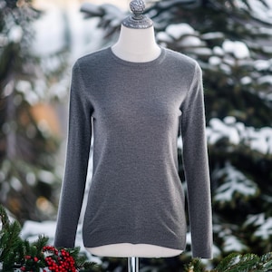 Peut inclure: Un pull gris à manches longues sur un mannequin. Le pull a un col rond et est fait d'un tissu doux et tricoté.
