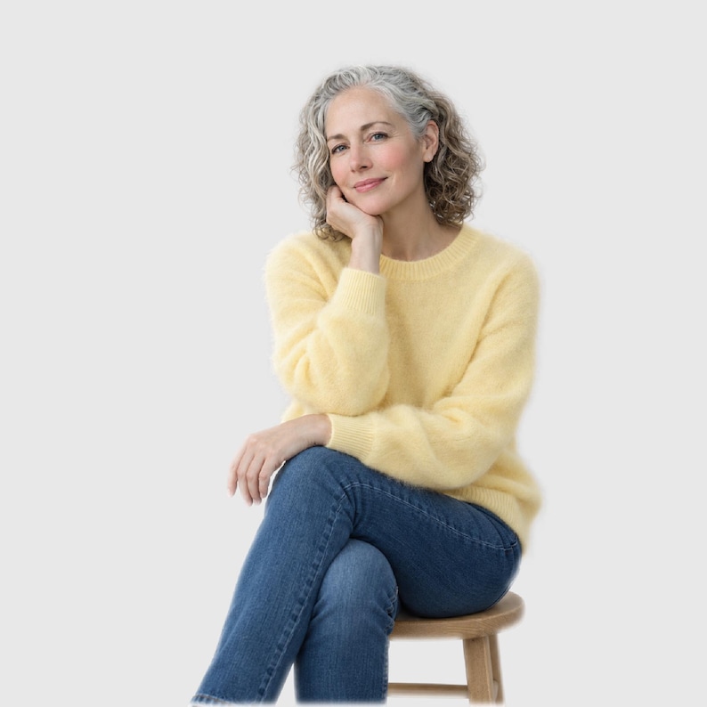 May include: A soft, pale yellow long-sleeved jumper with a crew neckline and a fuzzy, textured knit finish, paired with classic blue denim jeans. The jumper features ribbed cuffs and a ribbed hem, providing a simple and clean look.