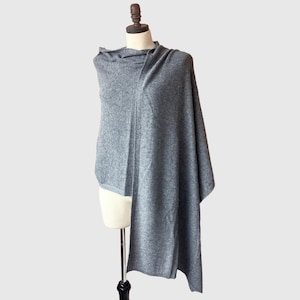May include: A gray shawl draped over a mannequin. The shawl is made of a soft, knitted material and has a draped design. The color is a medium gray, and the shawl appears to be warm and comfortable. The shawl is a versatile accessory.