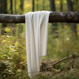 May include: A white knitted throw blanket draped over a tree branch in a forest setting.