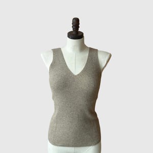 May include: A sleeveless ribbed knit top in a light brown color. The top has a v-neck and is fitted.