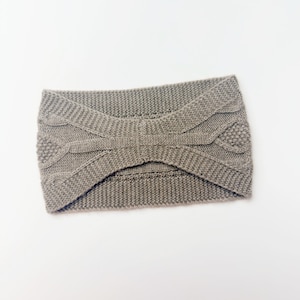 May include: A taupe-colored knitted headband with a cable-knit and textured design. The headband is made of a soft, warm material, perfect for keeping ears and forehead warm. The design features a central knot detail.