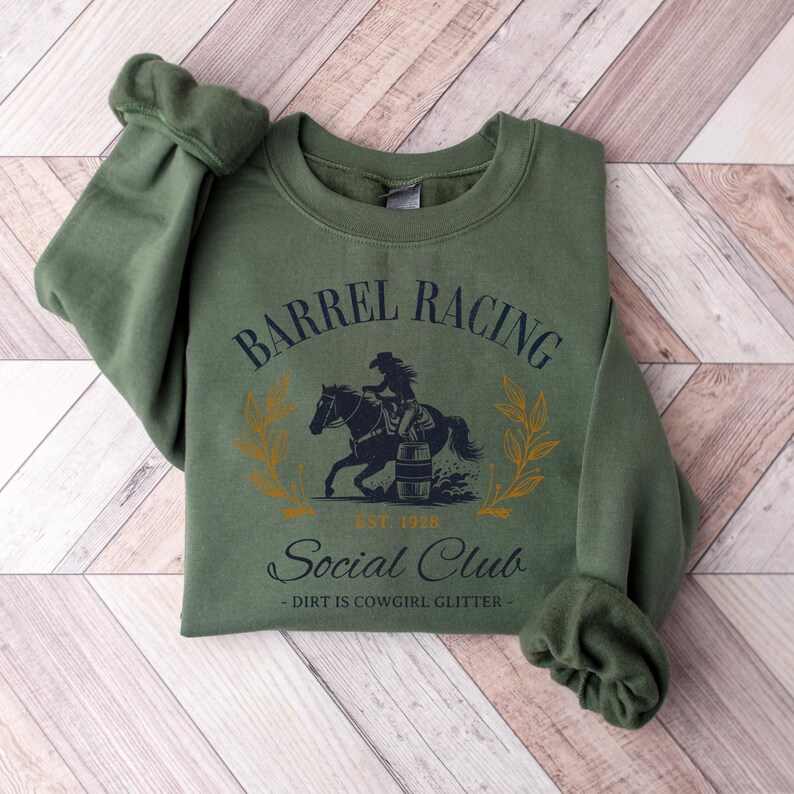 Pu&ograve; includere: Felpa verde con una stampa grafica di una cowgirl a cavallo e il testo "Barrel Racing Social Club - Dirt is Cowgirl Glitter - Est. 1928"
