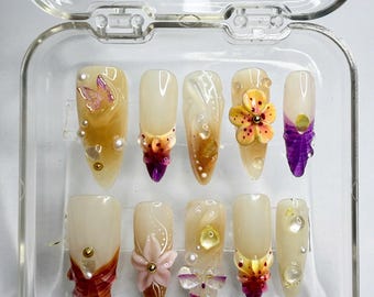 May include: A set of ten false nails with various floral and butterfly designs. The nails are in a clear plastic case.