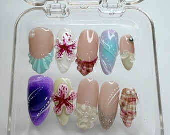 May include: A clear plastic box containing ten false fingernails with various designs. The designs include flowers, plaid, swirls, and polka dots. The nails are in different colors, including pink, white, blue, purple, and green.