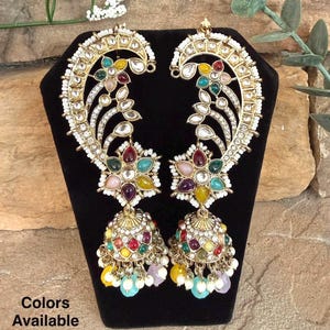 May include: A pair of ornate gold-toned earrings with colorful gemstones and dangling beads. The earrings feature a floral design with a mix of red, yellow, green, and blue stones. The text "Colors Available" is visible.
