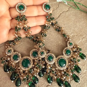 May include: A pair of large chandelier earrings featuring circular gold-tone frames set with round green cabochons and clear rhinestones. The design includes dangling green teardrop beads and clusters of small green and champagne-colored crystals.