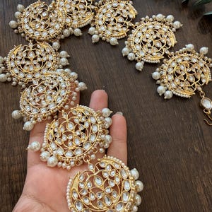 May include: A gold-toned hair accessory featuring multiple circular filigree medallions inlaid with clear stones. Each medallion is bordered by small white pearls, with additional pearl clusters dangling from the edges of the circular components.