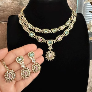 May include: A two-layer gold-tone necklace featuring alternating rectangular pastel pink and mint green stones set in ornate metal frames, with a matching pendant and a pair of drop earrings showcasing similar rectangular stones and floral-inspired accents.