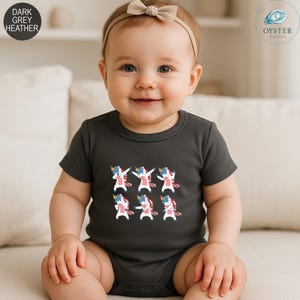May include: Dark grey heather baby bodysuit featuring a pattern of six cartoon unicorns in a dabbing pose. The unicorns have blue, red, and white accents. The bodysuit has short sleeves and a round neckline. The text "DARK GREY HEATHER" is in the upper left corner.