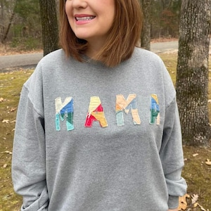 May include: Gray sweatshirt with the word "MAMA" spelled out in colorful patchwork fabric.