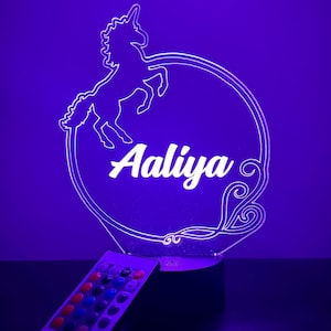 May include: A white unicorn silhouette with a circular outline and the name "Aaliya" inside. The light is on a black base and comes with a remote control with multiple colored buttons.