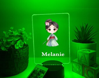 Könnte beinhalten: Personalisiertes LED-Nachtlicht mit einer Cartoon-Illustration eines Mädchens im Kimono, mit einer Blume im Haar. Der Name "Melanie" ist darunter aufgedruckt. Inklusive Fernbedienung und schwarzem Sockel.