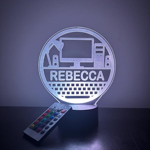 Peut inclure: Une veilleuse en acrylique blanche avec un motif d'ordinateur, de lampe de bureau et de clavier. Le nom "Rebecca" est imprimé sur la lumière. La lumière est sur une base noire et est livrée avec une télécommande.
