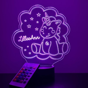 May include: A purple LED night light shaped like a cloud with a unicorn inside. The unicorn is sitting down with its legs crossed and has a crescent moon on its chest. The name "LileeAnn" is written on the cloud. The night light comes with a remote control.