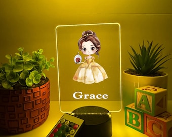 Könnte beinhalten: Personalisiertes LED-Nachtlicht mit einer Cartoon-Illustration einer Prinzessin, die eine Rose hält. Der Name "Grace" ist unter dem Bild aufgedruckt. Enthält eine Fernbedienung und einen schwarzen Sockel. Dekorative Pflanzen und ABC-Blöcke sind im Hintergrund.