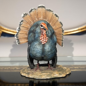 May include: A blue and brown ceramic turkey figurine with its tail feathers fanned out. The turkey is standing on a brown base.