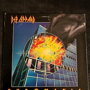 Könnte beinhalten: Das Albumcover von Def Leppards Pyromania. Das Bild zeigt eine Stadtlandschaft, die von einem Fadenkreuz anvisiert wird, mit einer feurigen Explosion in der Mitte. Das Logo der Band befindet sich oben, der Albumtitel unten.