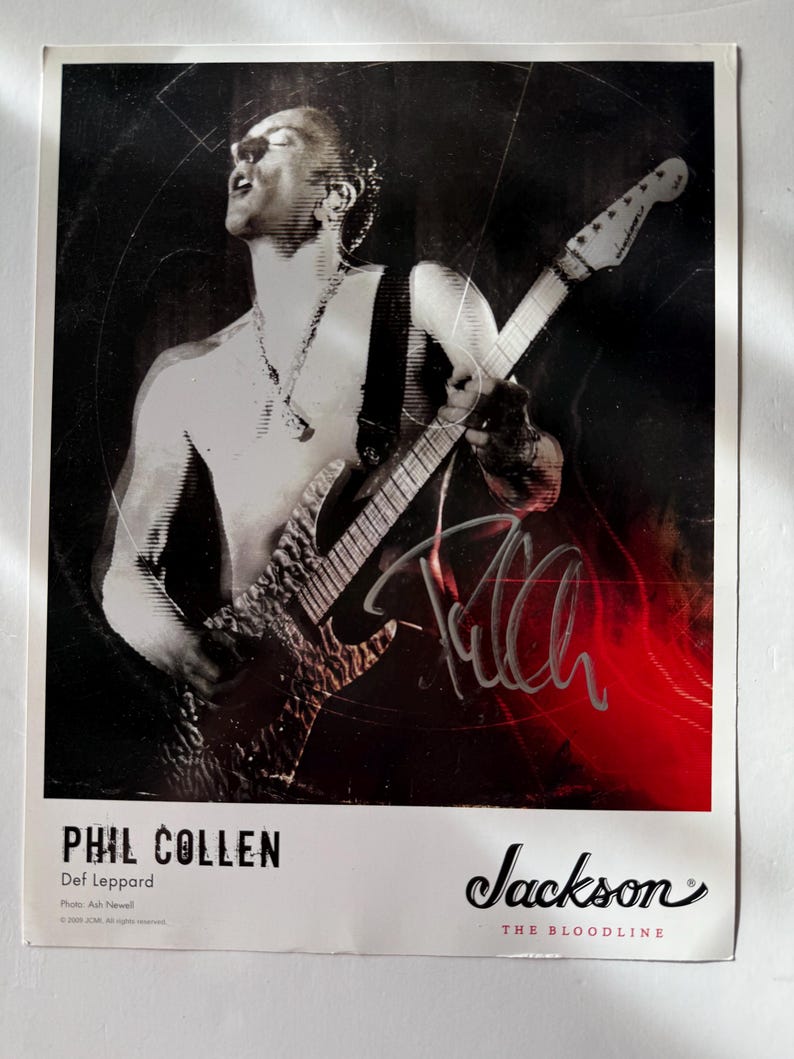 May include: A black and white poster featuring Phil Collen of Def Leppard playing a Jackson guitar. The image includes a signature, the text Phil Collen, Def Leppard, and the Jackson The Bloodline logo. The background has a red light effect.
