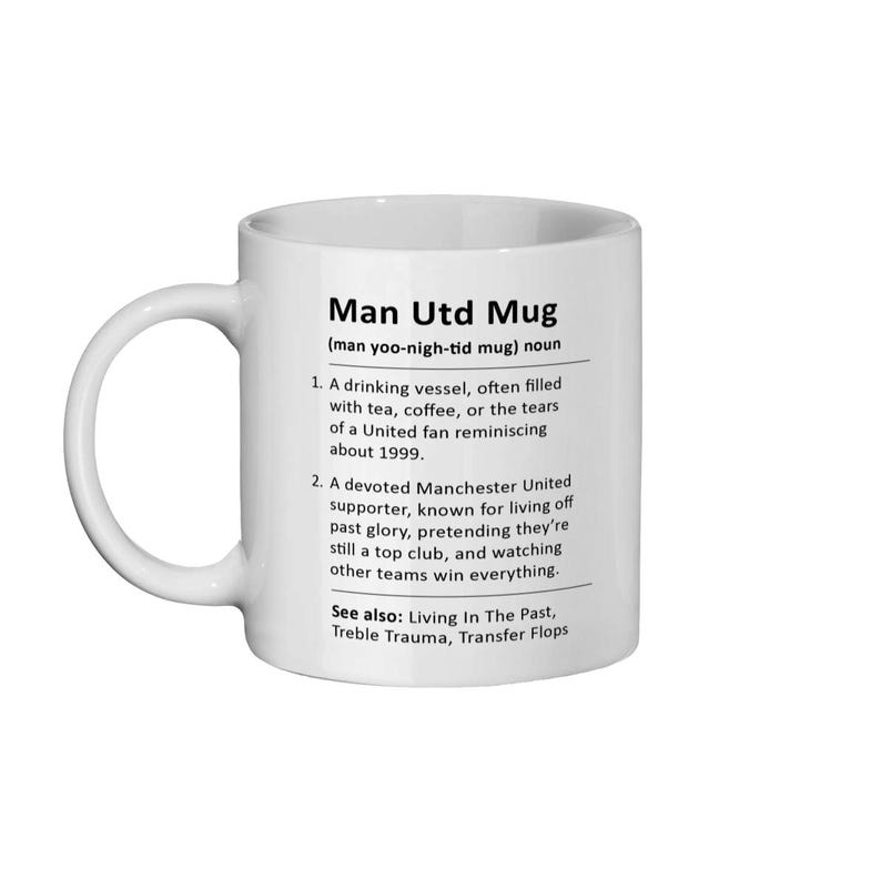 May include: White ceramic mug with a black design that defines "Man Utd Mug" as a drinking vessel often filled with tea, coffee, or tears of a United fan reminiscing about 1999. It also describes a devoted Manchester United supporter known for living off past glory, pretending they're still a top club, and watching other teams win everything. The text also includes "See also: Living In The Past, Treble Trauma, Transfer Flops."