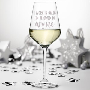 Puede incluir: Una copa de vino de vidrio transparente llena de vino blanco. La copa tiene el texto "I work in sales I'm allowed to wine" impreso en ella.