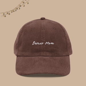 May include: A brown corduroy baseball cap with white embroidered text that reads "Berner Mom".
