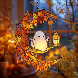 May include: A stained glass Halloween decoration featuring a crescent moon with autumn leaves in shades of orange, yellow, and purple. A cute ghost is on a swing, and a lantern hangs nearby. The decoration is suspended by a chain.