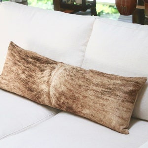 May include: A long, rectangular brown and white patterned throw pillow on a white couch.