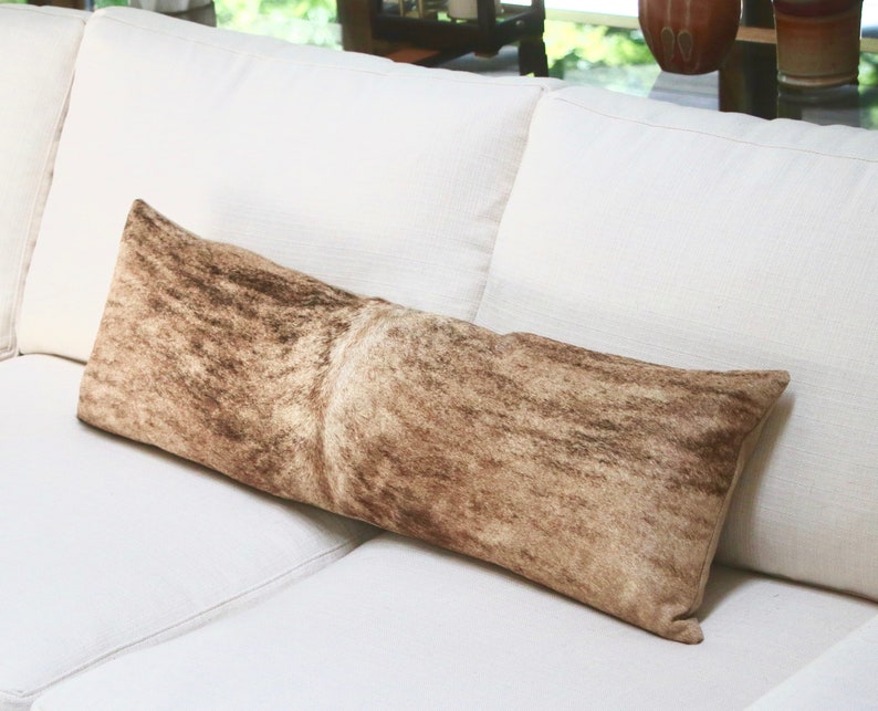 May include: A long, rectangular brown and white patterned throw pillow on a white couch.