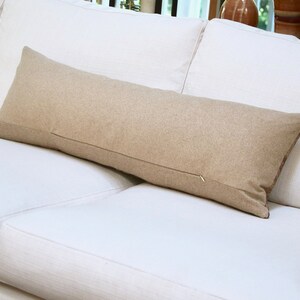 May include: A long, rectangular, beige throw pillow on a white couch.