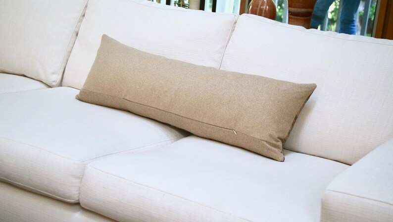 May include: A long, rectangular, beige throw pillow on a white couch.
