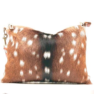 May include: A rectangular clutch bag with a brown and white spotted pattern. It features a zip closure and a gold-coloured chain. The bag is made of a soft, textured material and has a leather strap.