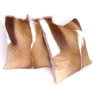May include: Two brown and white patterned throw pillows made from animal hide. The pillows are soft and fluffy and would add a touch of rustic elegance to any room.