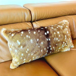 May include: A rectangular decorative pillow with a spotted pattern in shades of brown and white. The pillow is placed on a brown leather sofa, creating a cozy and inviting aesthetic. The pillow's texture adds visual interest.