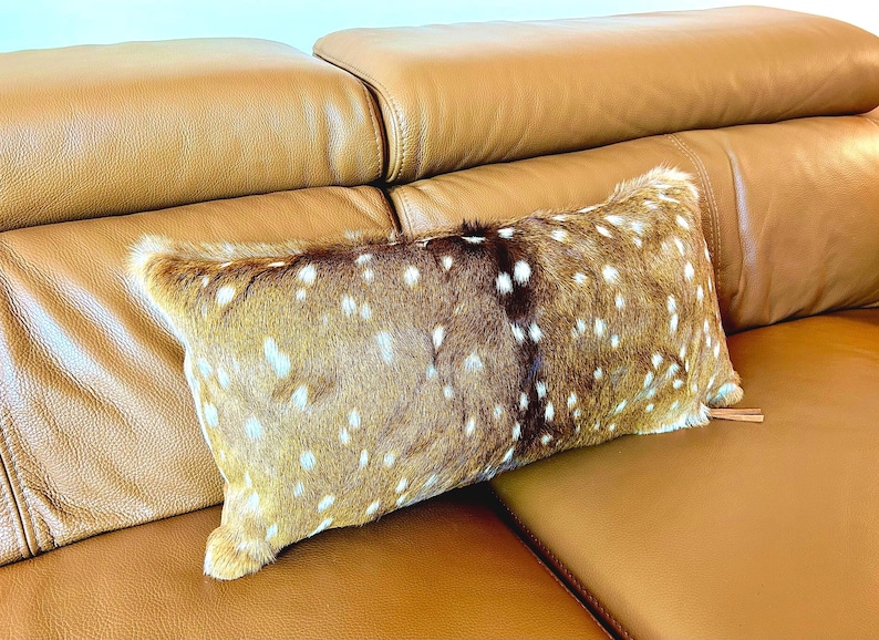 May include: A rectangular decorative pillow with a spotted pattern in shades of brown and white. The pillow is placed on a brown leather sofa, creating a cozy and inviting aesthetic. The pillow's texture adds visual interest.