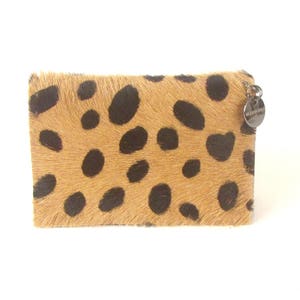 May include: A tan and black leopard print wallet with a silver metal charm that says "Mi Casa es Su Casa".