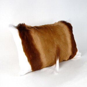 May include: A brown and white fur pillow with a long, white tail hanging down. The pillow is made of real animal fur and has a soft, luxurious feel.
