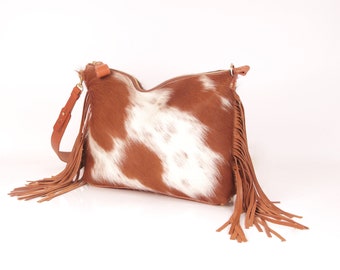 May include: A brown and white cowhide handbag with a long fringe strap.