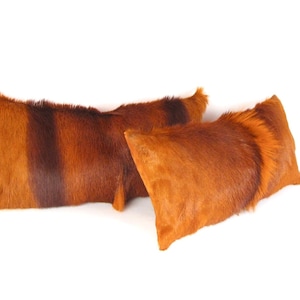 May include: Two long rectangular pillows covered in brown and orange cowhide.