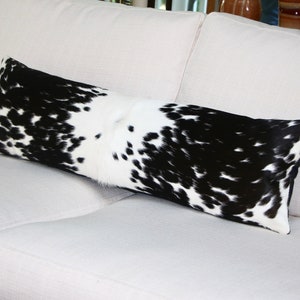 May include: A black and white cowhide lumbar pillow on a white couch.