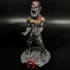 May include: A detailed figurine of a character with a bald head, a long gray beard, and red markings on his face and chest. The figure is in a battle stance, with arms outstretched. It stands on a gray stone base with a red Omega symbol.