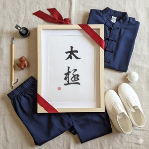 Può includere: Un assortimento di articoli relativi al Tai Chi, tra cui una stampa calligrafica incorniciata con i caratteri "太極", abbigliamento blu navy, scarpe bianche, un pennello, inchiostro e un nastro rosso.