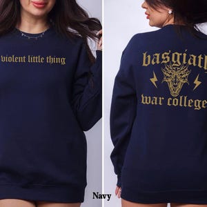Pode incluir: Camisola azul marinho com um gr&aacute;fico de drag&atilde;o dourado e o texto "basgiath war college" nas costas. A frente da camisola tem o texto "violent little thing" em dourado.