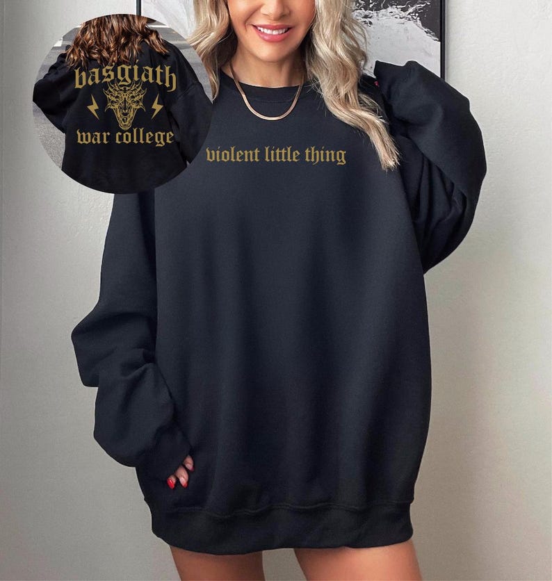 Pode incluir: Camisola de moletom preta oversized com o texto "violent little thing" em letras douradas. A camisola tem gola redonda e mangas compridas.