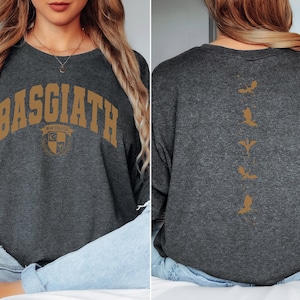 Op de afbeelding: Een donkergrijs sweatshirt met de tekst "BASGIATH" in gouden letters op de voorkant en een reeks gouden vogelsilhouetten op de achterkant.